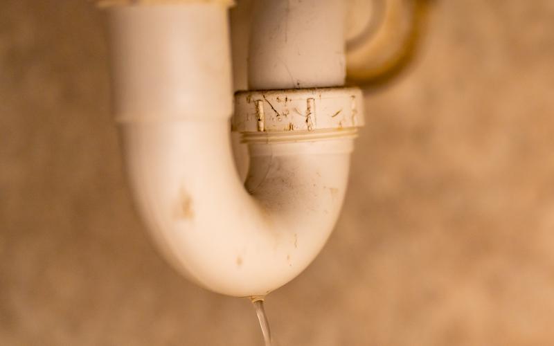 White drain trap under a sink with water dripping from the bottom